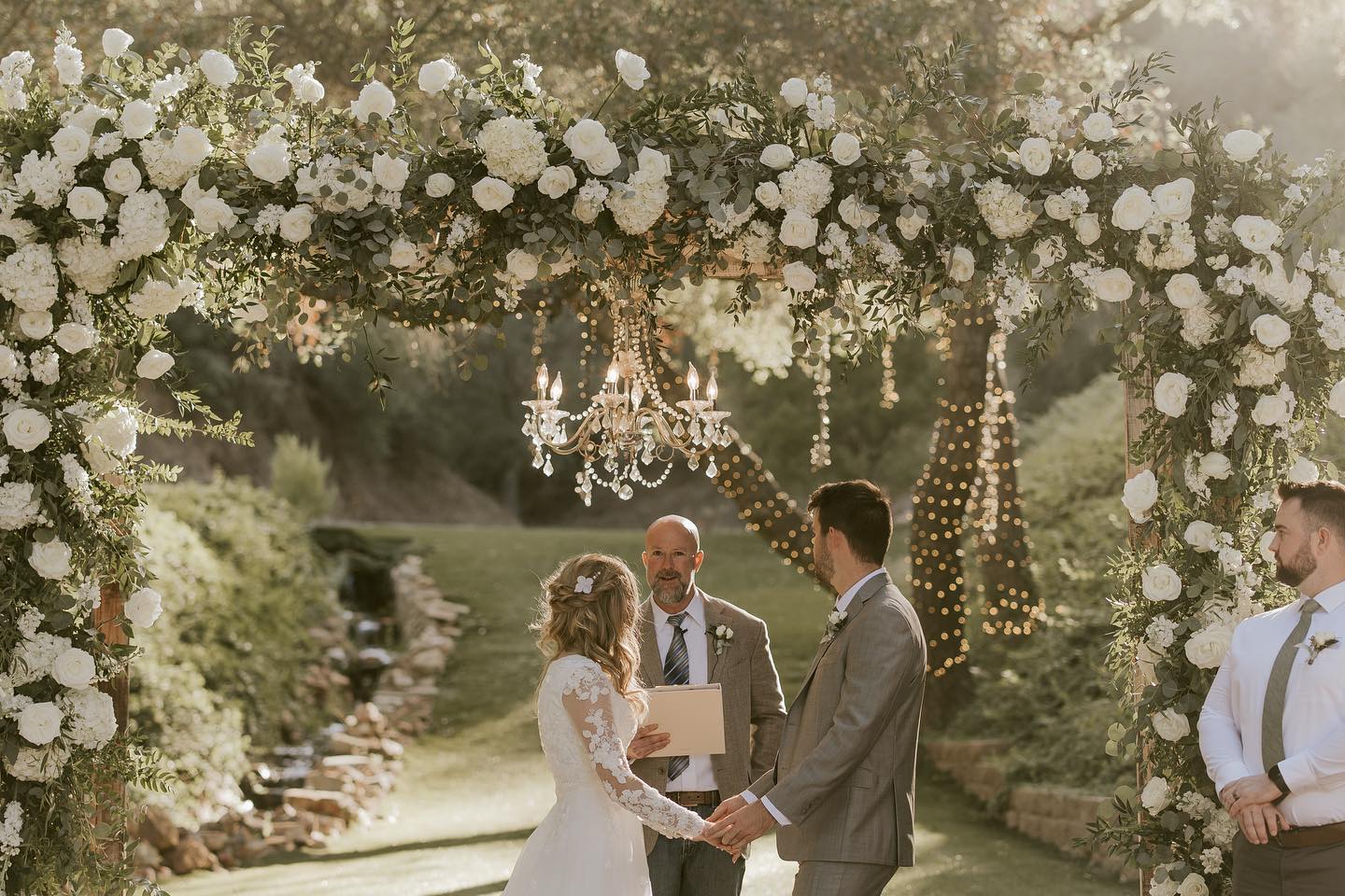 bride and groom under large floral arch
